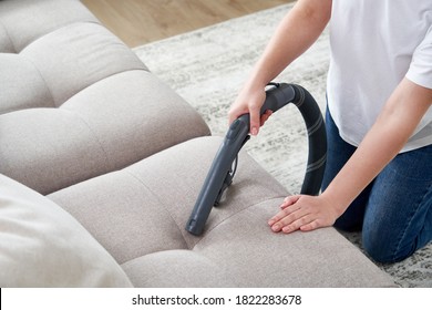 Young housewife Cleaning Sofa with Vacuum Cleaner in living room