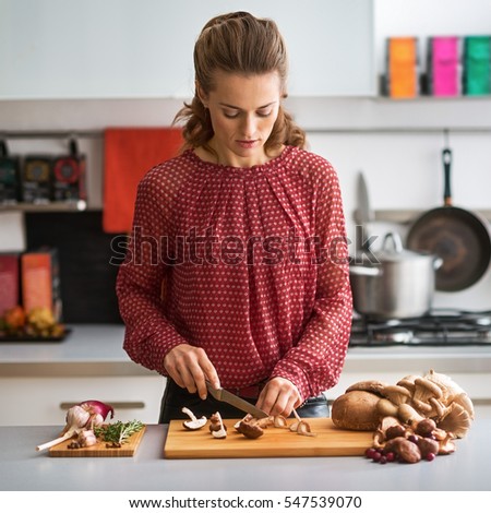 Young housewife cutting mushrooms in kitchen