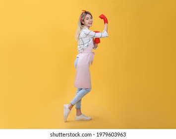 Young housewife in gloves on yellow background - Shutterstock ID 1979603963