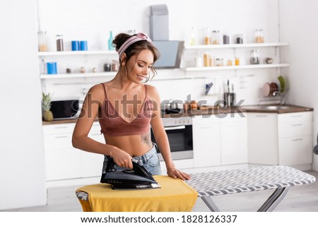 Young housewife in headband ironing t-shirt at home