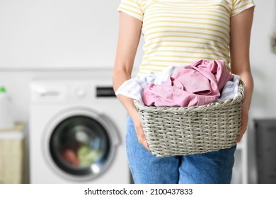 Young housewife holding wicker basket with laundry at home