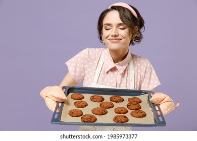 Young Housewife Housekeeper Chef Cook Baker Woman Wearing Pink Apron Showing Chocolate Cookies Biscuits On Baking Sheet Sniff Chocolate Smell Isolated On Pastel Violet Background. Cooking Food Concept
