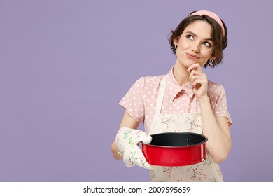 Young Housewife Housekeeper Chef Cook Baker Woman In Pink Apron Hold Red Non-stick Baking Form For Pie Cake Look Aside Prop Up Chin Isolated On Pastel Violet Background Cooking Food Process Concept