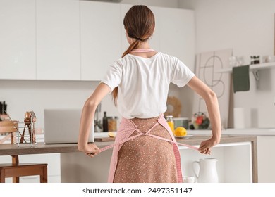 Young housewife tying apron in kitchen, back view - Powered by Shutterstock