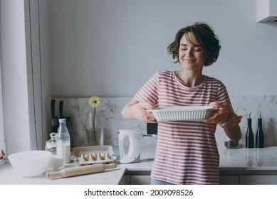 Young Housewife Woman 20s In Casual Clothes Striped T-shirt Holding Hot Casserole In Baking Dish Sniff Delicious Scent Cooking Food In Light Kitchen At Home Alone Healthy Diet Bakery Lifestyle Concept