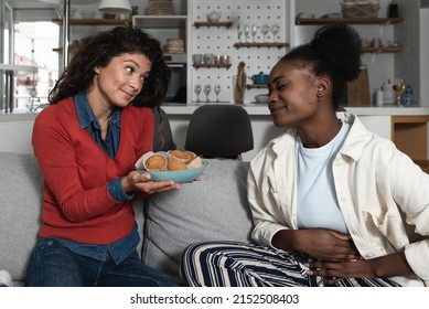 Young Hungry African American Woman Is On Diet And Her Friend And Roommate Offering To Her A Muffins To Eat. Dieting And Hunger Healthy Eating Concept.