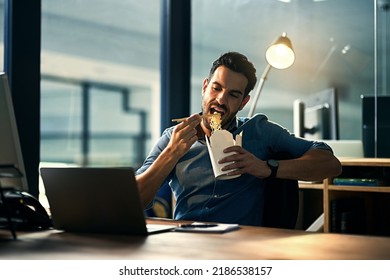 Young hungry businessman working late and eating at desk. Man having takeout food in the office at work station in the evening. Male entrepreneur eating asian meal during the night at the workplace - Powered by Shutterstock