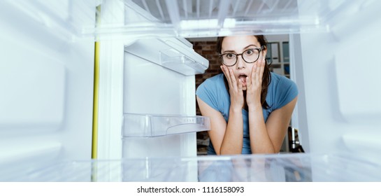 Young Hungry Desperate Woman Looking Into Her Empty Fridge, She Is Panicking