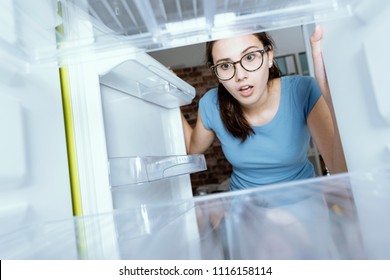 Young Hungry Desperate Woman Looking Into Her Empty Fridge, She Is Panicking