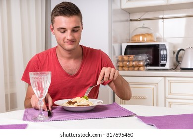 Young Hungry Man Digging Into Plate of Pasta While Seated at Dining Table in Quaint Kitchen at Dinner Time
