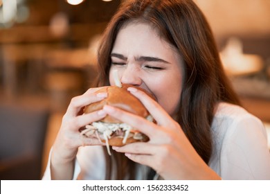 Young Hungry Woman In White Stylish Blouse Biting With Appetite Fresh Meat Burger During Lunch In Trendy Resturant Eating Outside.