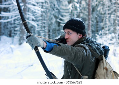 Young hunter with bow and arrows in the winter forest