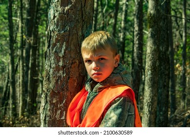 A young hunter in orange standing in the woods next to a pine tree- hunting- deer woods- hunting season in the forest- young boy waiting for a deer- hunting and gun safety