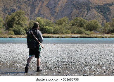 Young Hunter With A Rifle Crossing Mountain River, New Zealand