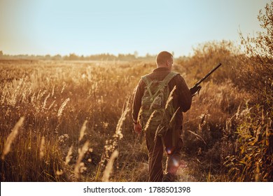 Young hunter in the sunny field with military backpack and shotgun waiting for flying ducks