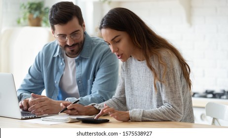 Young husband and wife using calculator laptop computer manage finances calculate bills tax talk doing paperwork together sit at home table discuss family mortgage loan money payment planning budget