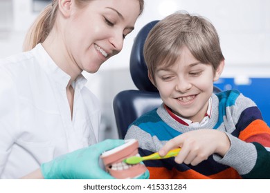Young hygienist holding a jaw model, instructing a little boy how to brush teeth correctly - Powered by Shutterstock