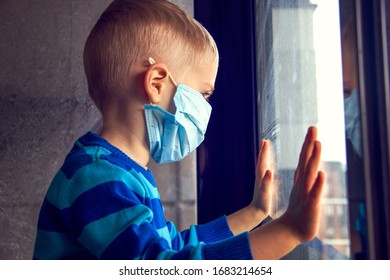 Young Ill Boy At The Hospital Looks At Window And Wants To Go Home. Kid Using The Medical Face Mask . Protection Against Corona Virus. Sick Child Breathes Through A Protective Mask