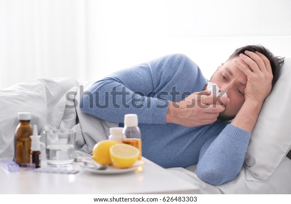 Young ill man lying in bed\
at home