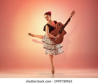 Young and incredibly beautiful ballerina as spaniard in pointe shoes is posing and dancing flamenco in a red studio. Classical ballet and art concept. Spanish temperament and passion in dance