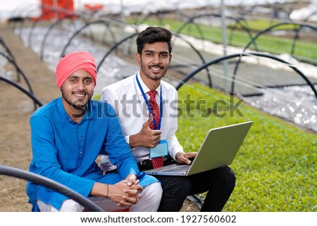 Young indian agronomist showing some information to farmer in laptop at greenhouse