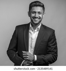 Young Indian Asian Man Wearing Black Suit And White Shirt Over Isolated Grey Or White Background Happy Face Smiling With Crossed Arms Looking At The Camera. Positive Person. Black And White.