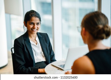 A Young Indian Asian Woman Has A Business Meeting (interview) With A Caucasian White Woman In An Office During The Day. They Are Both Young, Attractive And Professionally Dressed. 