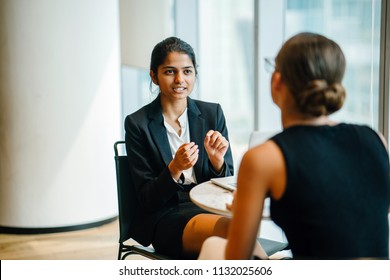 A Young Indian Asian Woman Has A Business Meeting (interview) With A Caucasian White Woman In An Office During The Day. They Are Both Young, Attractive And Professionally Dressed. 