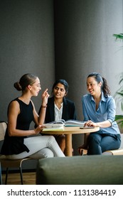 A young Indian Asian woman is having a business meeting with her team in a meeting room. Her team of colleagues is diverse with a Caucasian brunette woman and a Chinese Asian woman. 
