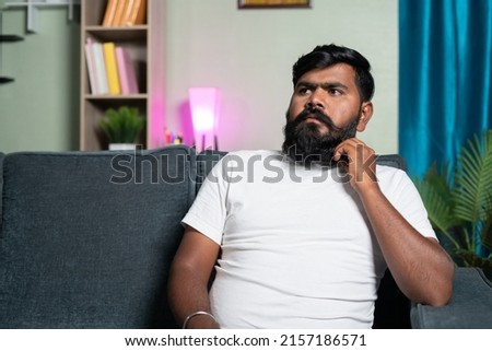 young indian beardman thinking or day dreaming while sitting on sofa at home - concept of thoughtful, wasting of time and doubtful. Stock photo © 