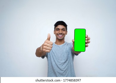 Young indian boy holding a phone with green screen, showing thumbs up in the background.