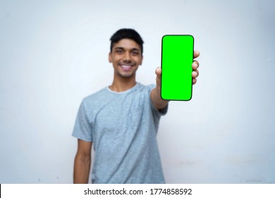 Young indian boy holding a phone with green screen, showing thumbs up in the background. - Powered by Shutterstock