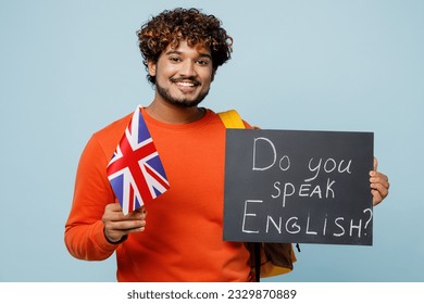 Young Indian boy student wear casual clothes bag hold British flag card with text do you speak english travel abroad to study isolated on plain blue background High school university college concept