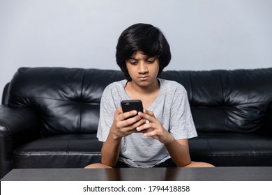 Young Indian Boy Using Mobile Phone As He Sits On Couch At Home.