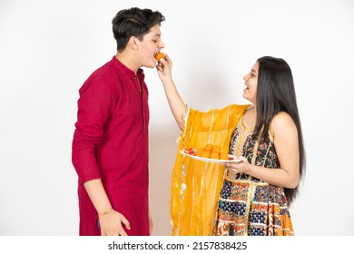 Young Indian brother and sister celebrating Diwali, rakshabandhan or bhai dooj festival isolated on white studio background. enjoying sweet laddo,