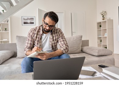 Young Indian Business Man Student Or Remote Employee Wearing Glasses Working Online From Home Office, Edistance Learning Using Laptop Computer Watching Remote Webinar Training Class, Taking Notes.