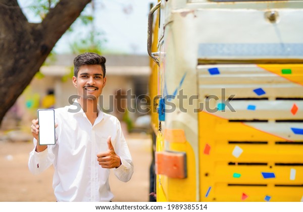 Young indian businessman with his\
freight forward lorry or truck and showing\
smartphone.