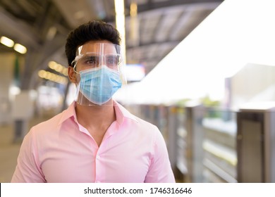Young Indian businessman with mask and face shield waiting at the sky train station
