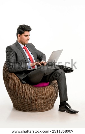 Young indian Businessman sitting on chair and using laptop on white background.