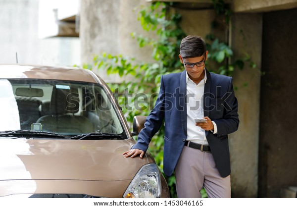 Young Indian businessman standing out side of car\
and Using mobile phone