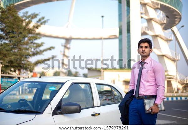 Young Indian businessman\
with tablet in hand standing near car , Businessman and Employee\
concept