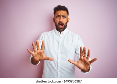 Young indian businessman wearing elegant shirt standing over isolated pink background afraid and terrified with fear expression stop gesture with hands, shouting in shock. Panic concept.