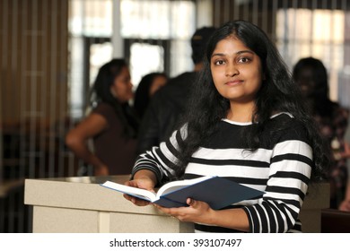 Young Indian college student holding book inside campus