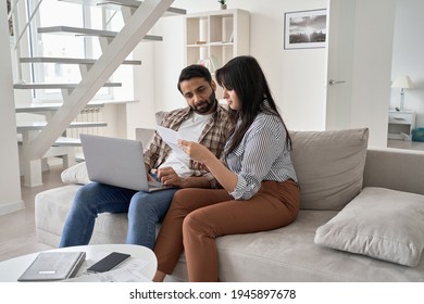 Young indian couple checking paper bills paying mortgage loan bank debt online together on computer, calculating taxes, expenses, making payments, planning family budget finances using laptop at home. - Powered by Shutterstock