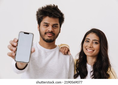 Young Indian Couple Laughing While Showing Mobile Phone Isolated Over White Background