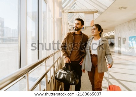 Young indian couple looking in window together at airport indoors