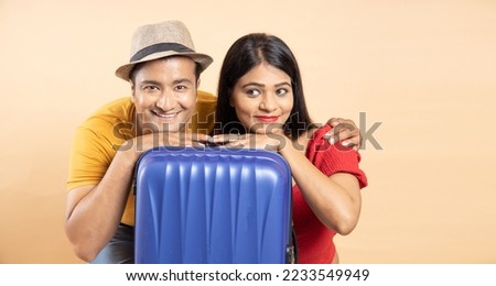 Young Indian couple with travel trolley bag luggage ready to go on vacation holiday traveling trip, isolated over beige background, copy space, studio shots. Closeup, honeymoon