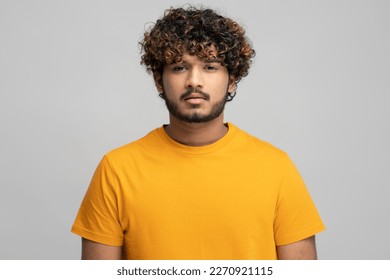 Young Indian curly-haired bearded man, wearing bright yellow t-shirt looking confidently at camera over isolated gray background. Portrait of Asian pensive and confident young student - Powered by Shutterstock