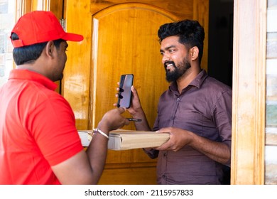 young indian customer showing mobile after paying to delivery boy by scanning qr code on mobile phone at door step - concept of contectless or cashless payment,technology and shipment service.