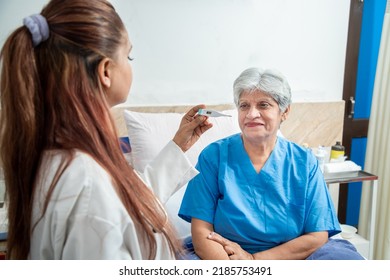 Young Indian Doctor Check Fever Of Old Senior Female Patient Using Thermometer At Hospital Or Clinic. Elderly People Health Care Concept.